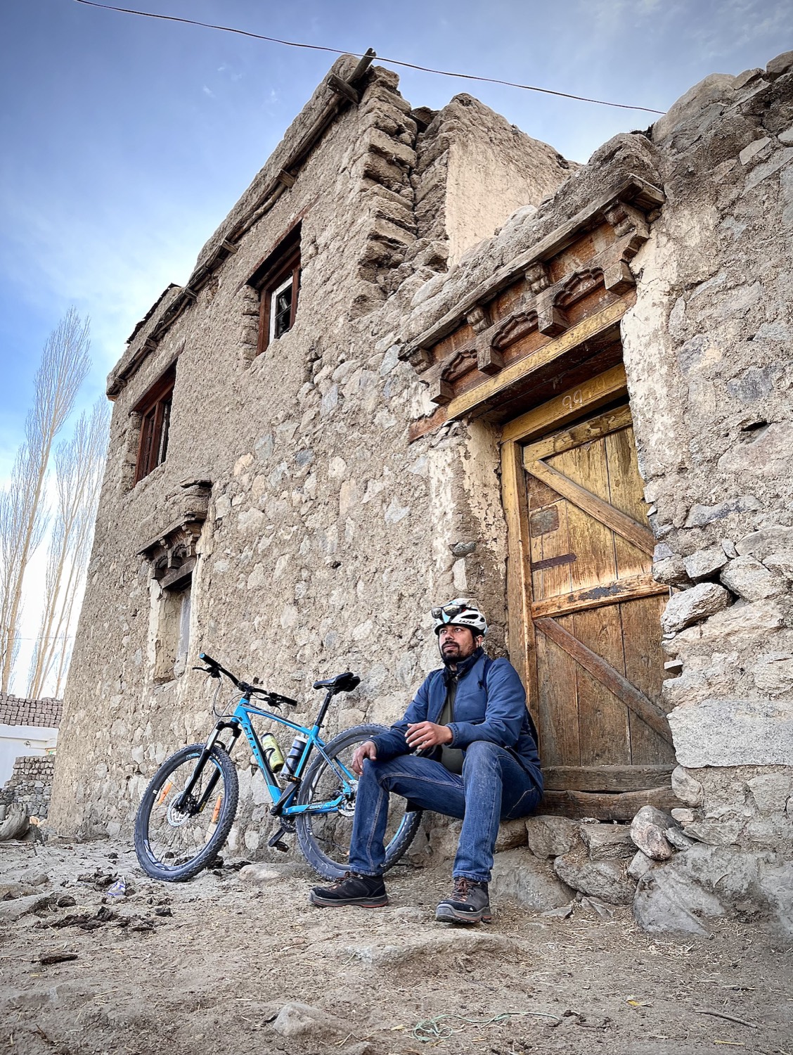 Sandeep resting with a mountain bike outside an old stone house in Ladakh