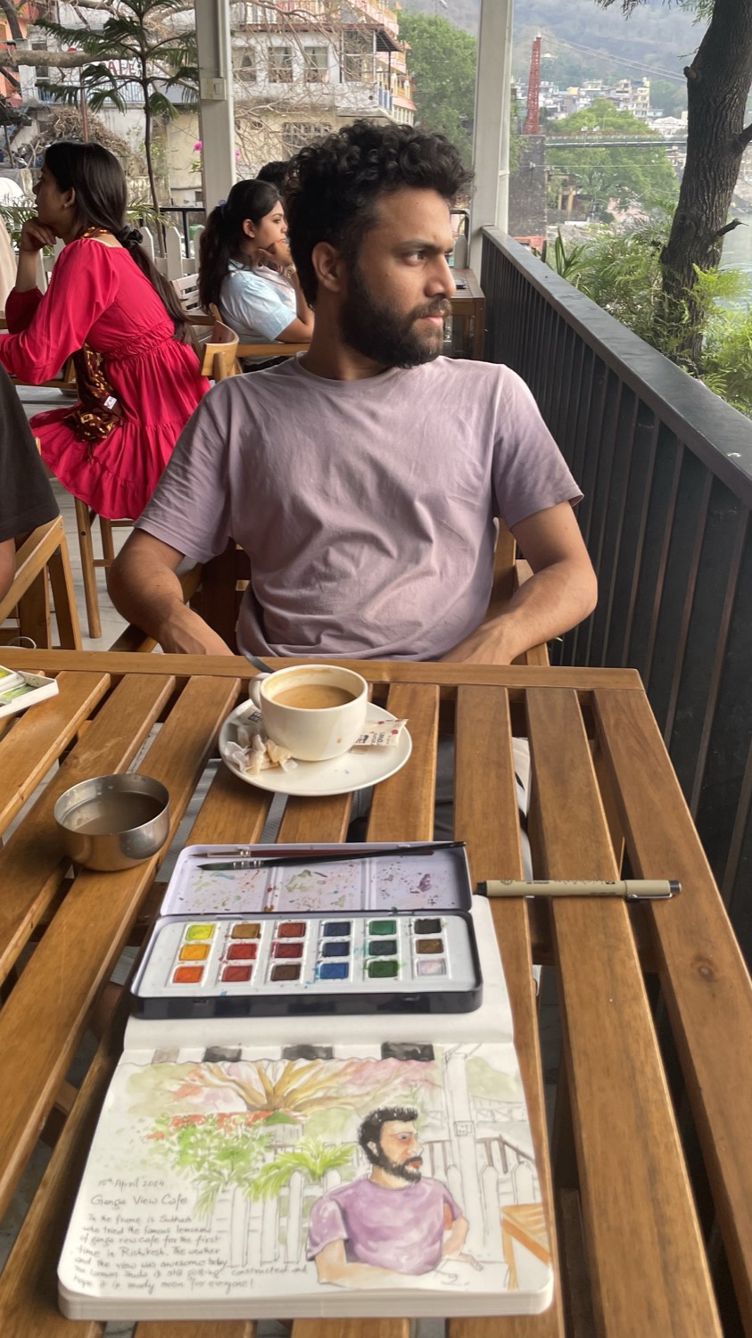 Sandeep at the Ganga View Café in Rishikesh, his watercolour kit open and a painting of himself drying on the page